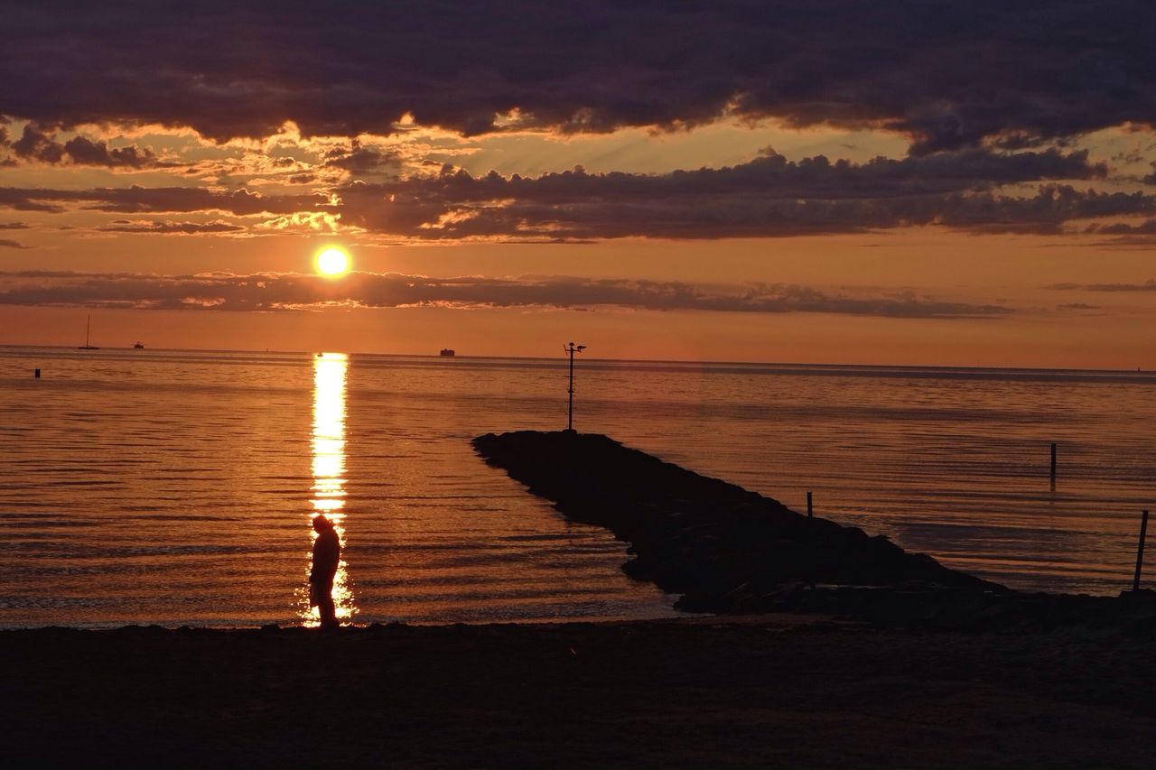 Silhouette person standing on beach against orange sky