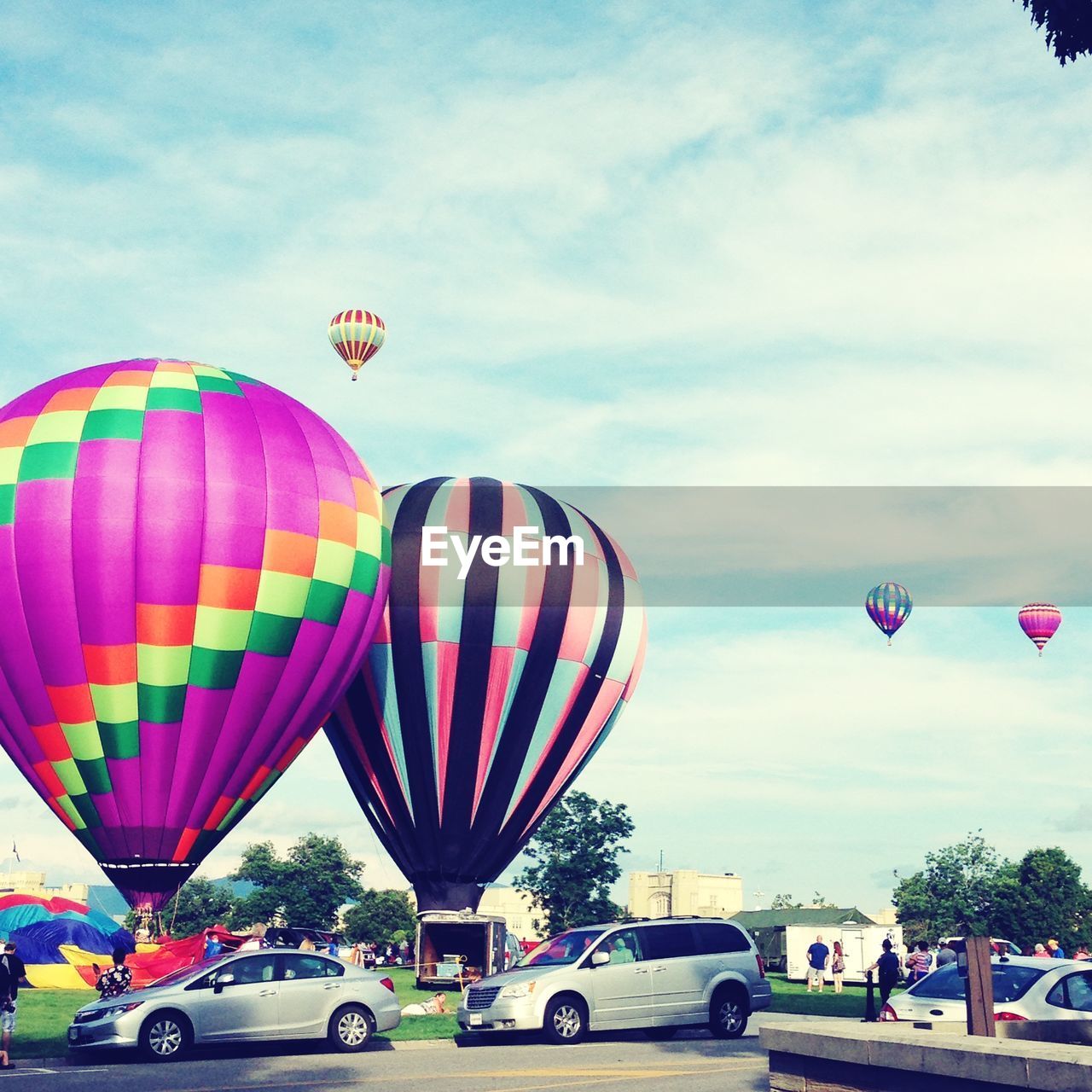 Multi colored hot air balloons on field by cars against sky