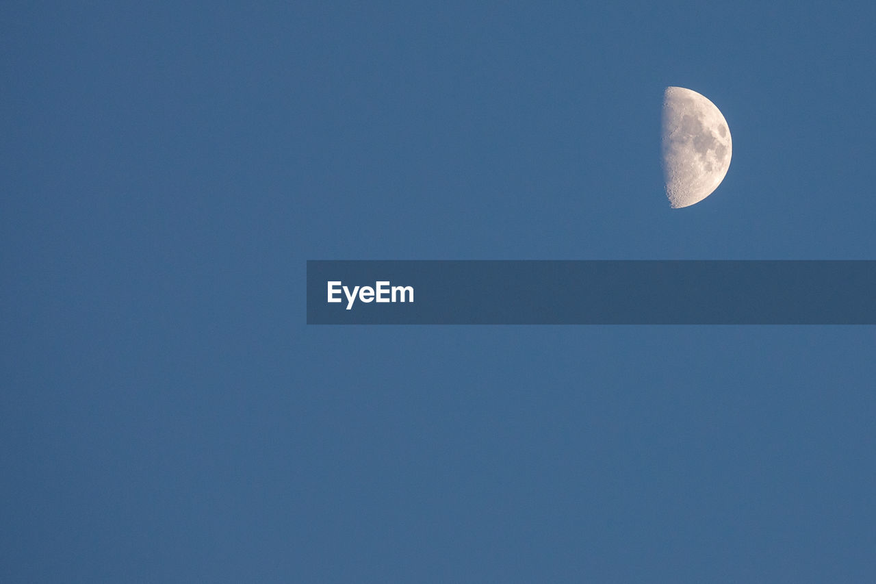 Low angle view of half moon in clear blue sky at dusk