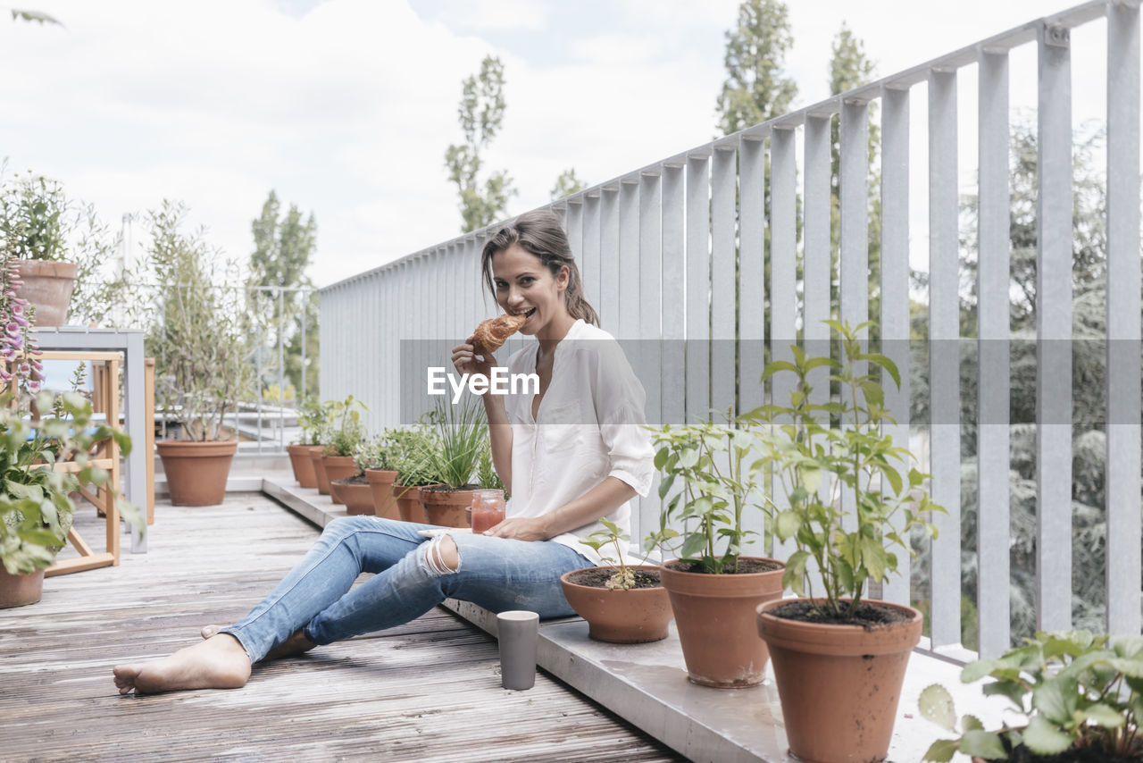 Smiling woman eating croissant with jam on balcony