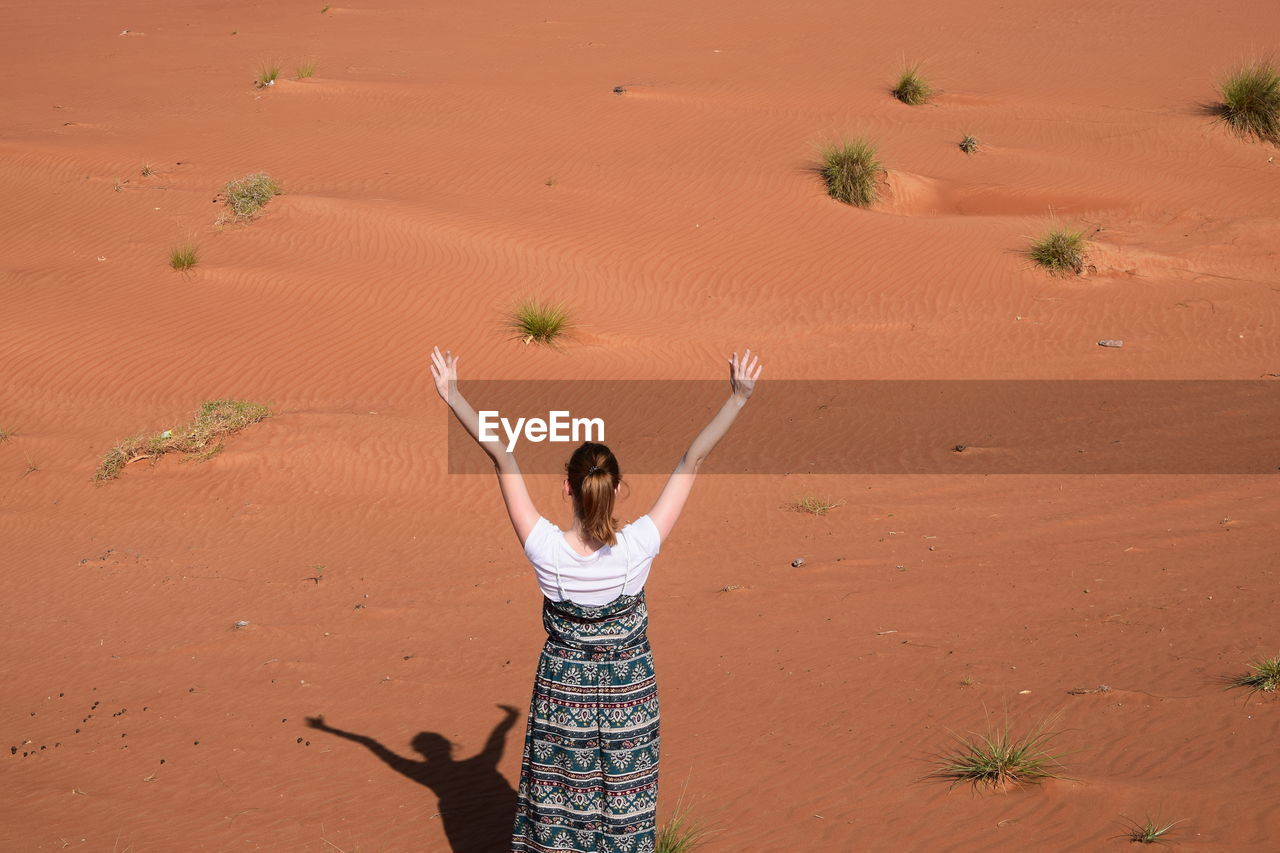 Rear view of woman standing with arms raised in desert on sunny day