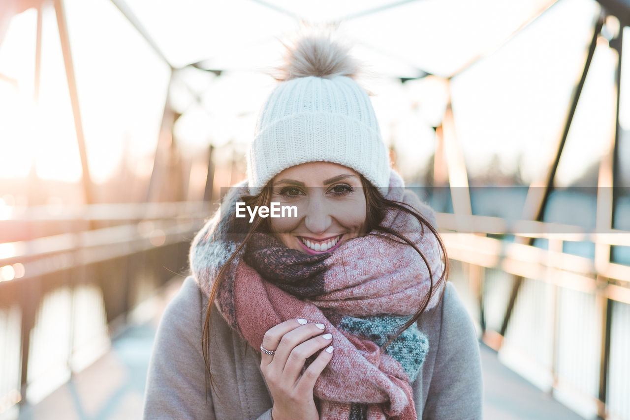 Portrait of smiling young woman wearing warm clothing on bridge