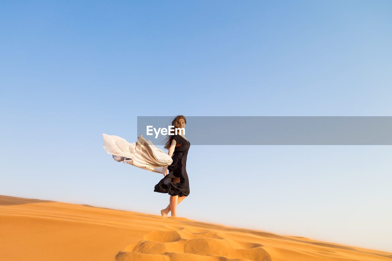 Full length of woman standing on sand dune against clear sky