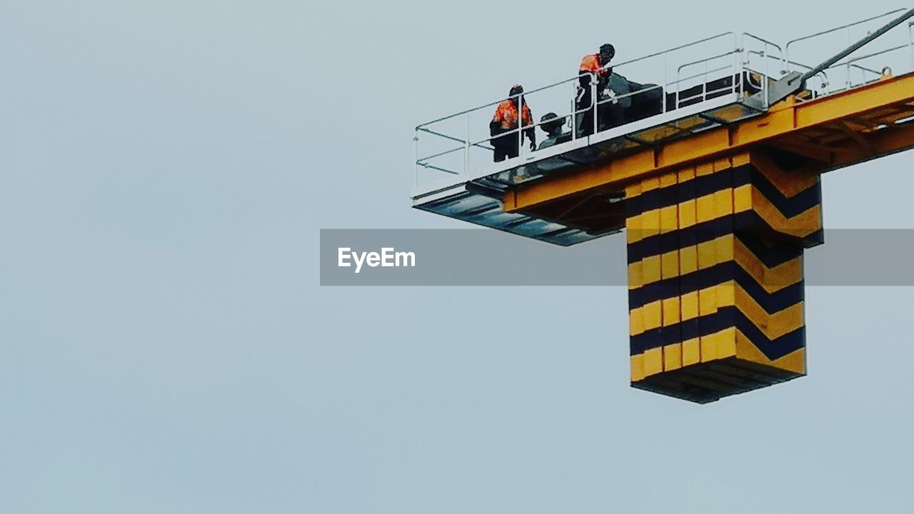 LOW ANGLE VIEW OF MEN WORKING AT CONSTRUCTION SITE AGAINST SKY