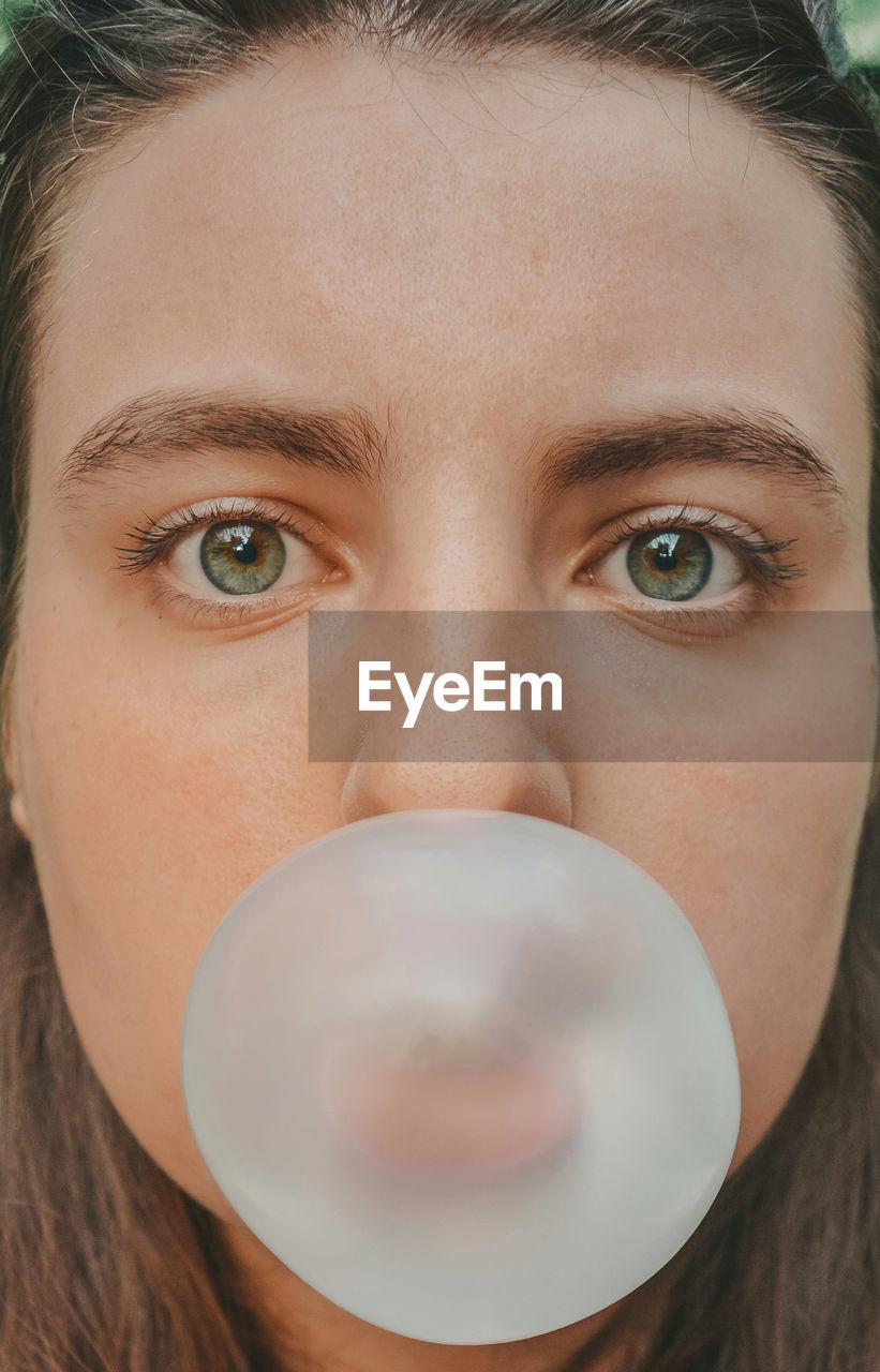 Close-up portrait of young woman blowing bubble