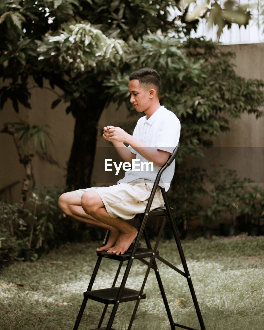 Side view of young man sitting on chair in yard