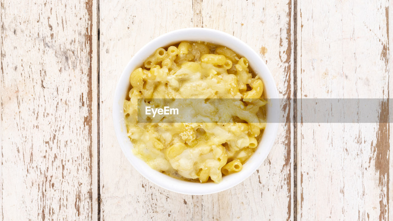 Mac and cheese, macaroni pasta with cheese in ceramic bowl on white old wood texture background