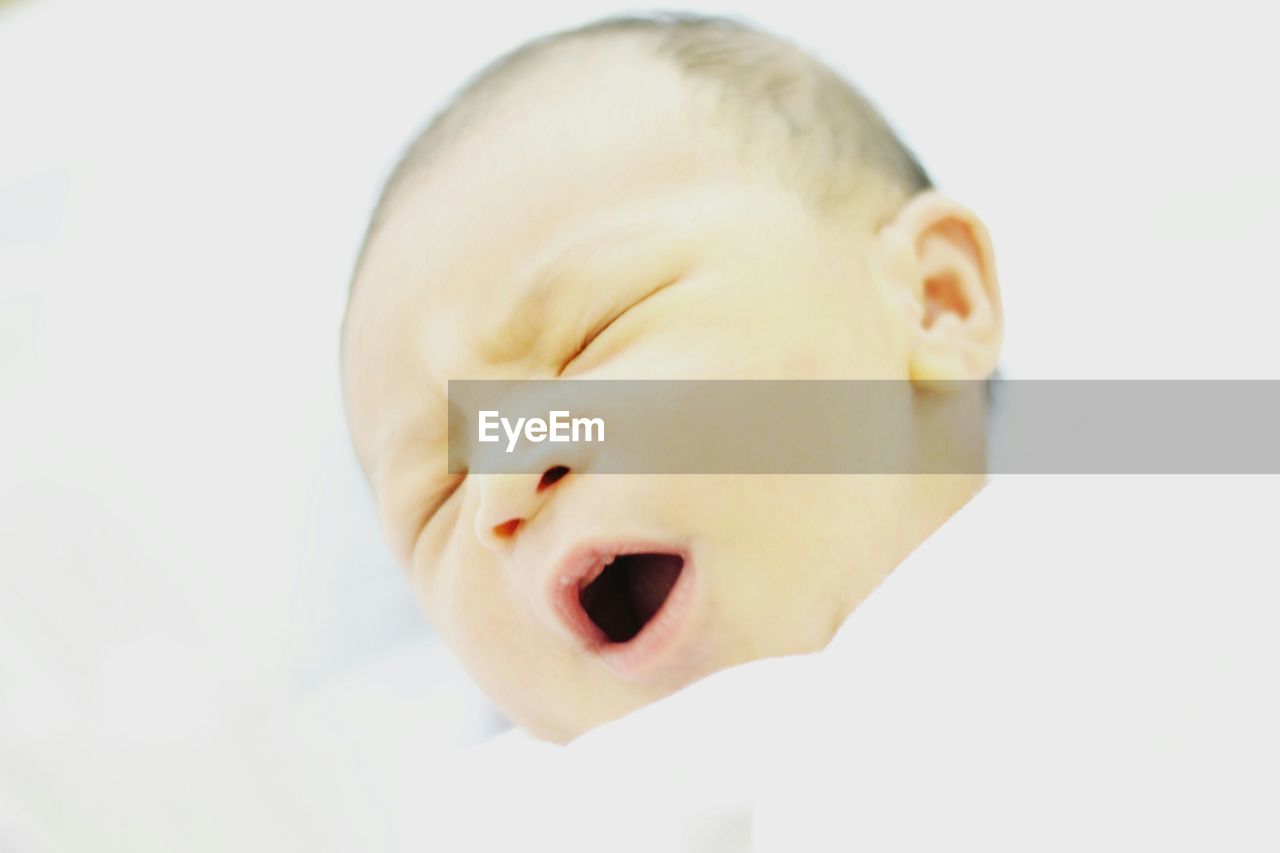 Close-up of infant baby yawning against white background