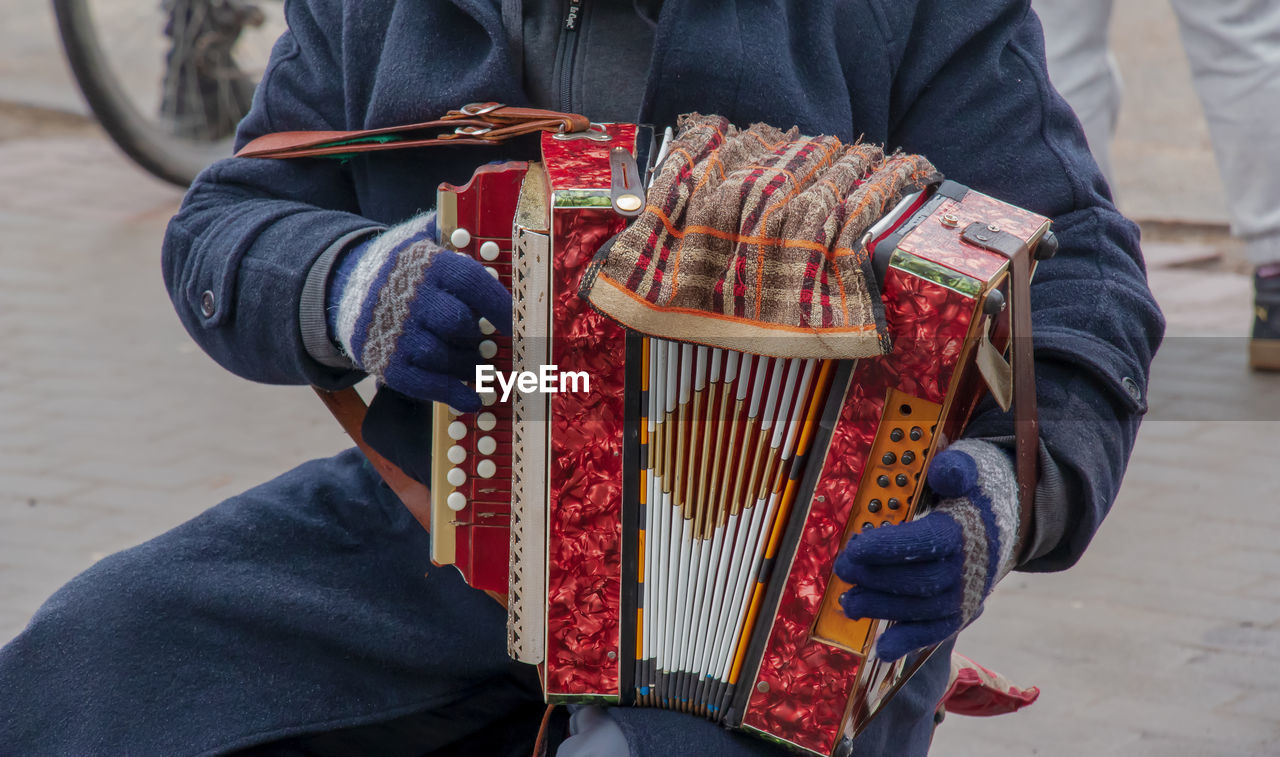 Close-up of a man's hand playing button accordion outdoors in winter.
