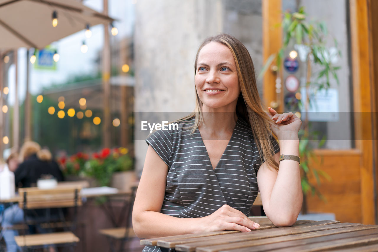 Confident young woman sitting in a street cafe at a table in a gray striped