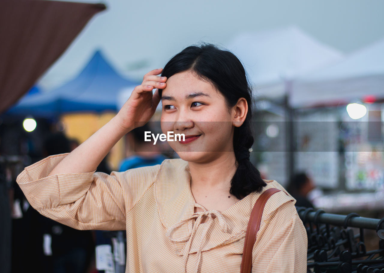 Smiling young woman looking away while standing against sky