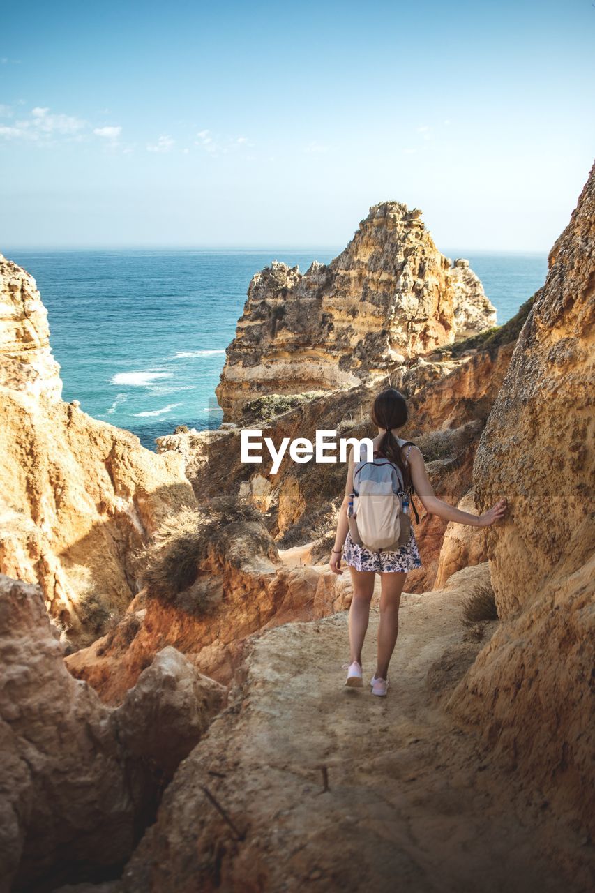 Rear view of woman standing on rock by sea against sky