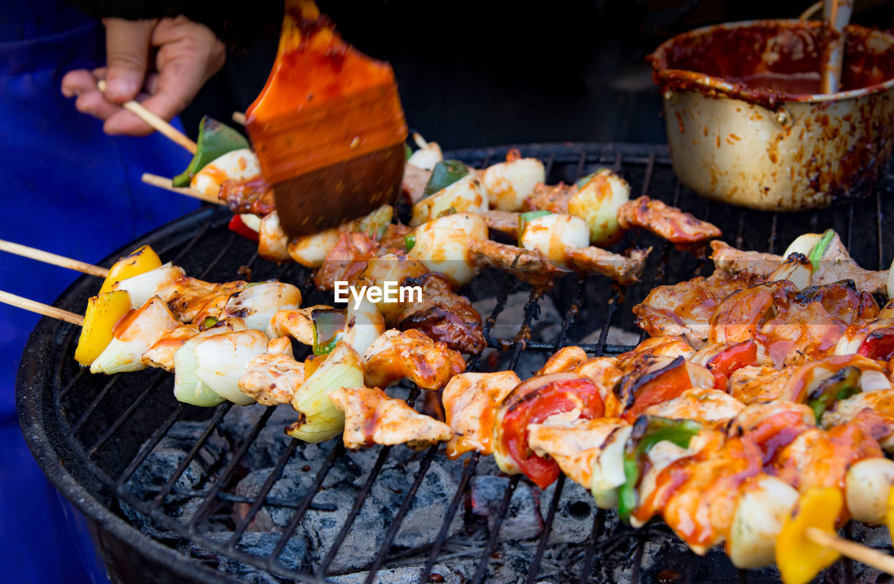 CLOSE-UP OF PERSON PREPARING FOOD ON BARBECUE