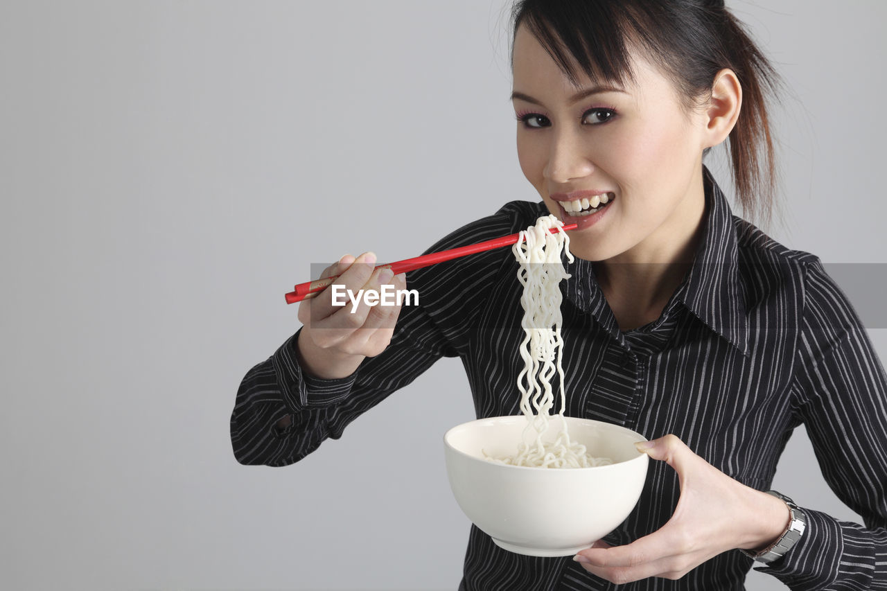 Portrait of woman eating noodles with chopsticks against white background