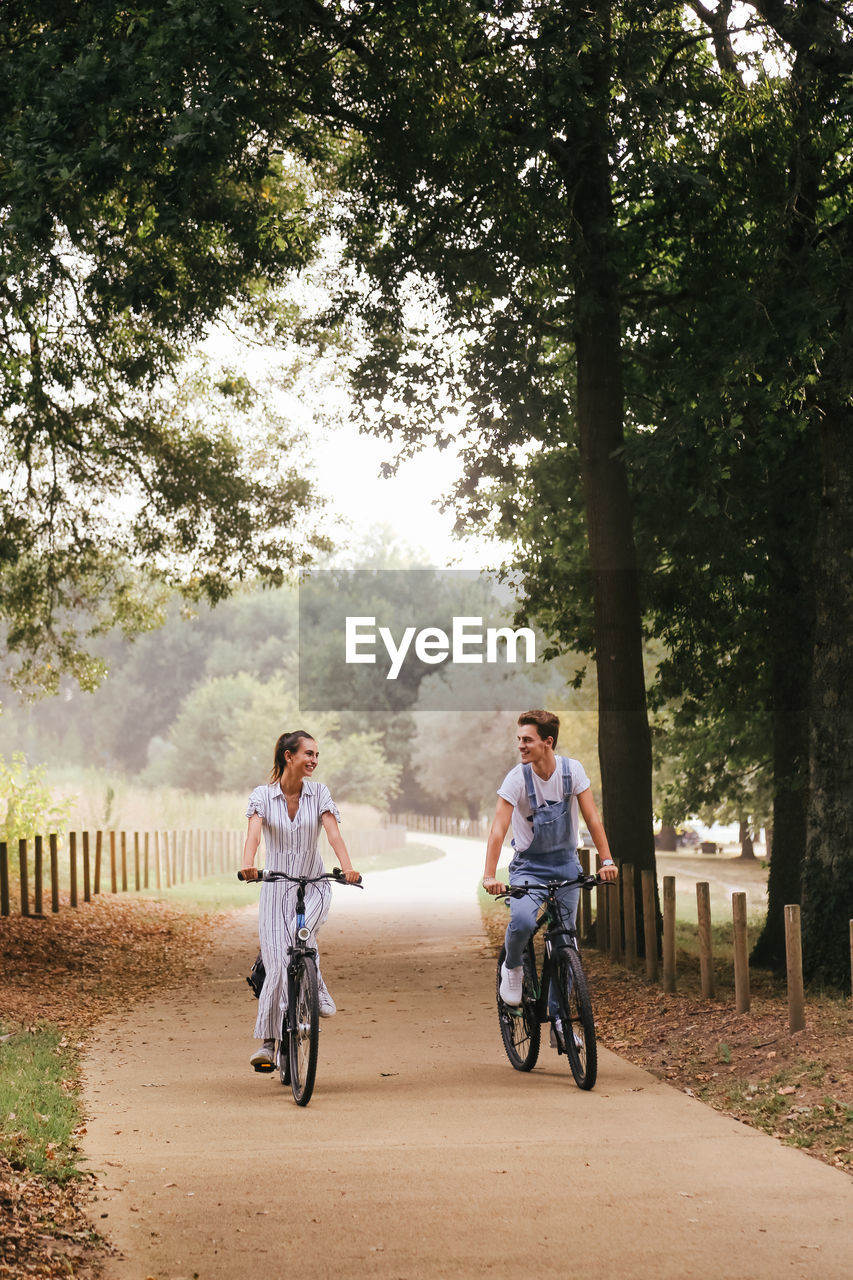 Couple riding bicycles on dirt road amidst trees