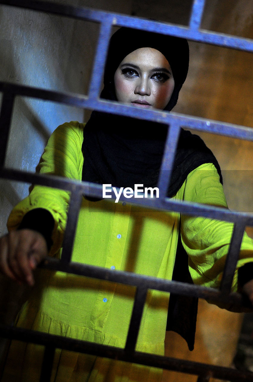 Portrait of woman standing by metal grate