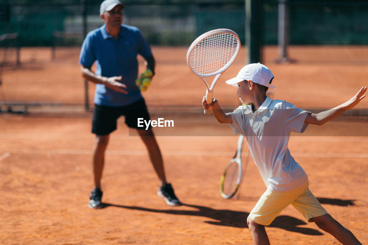 Coach teaching tennis to boy at court