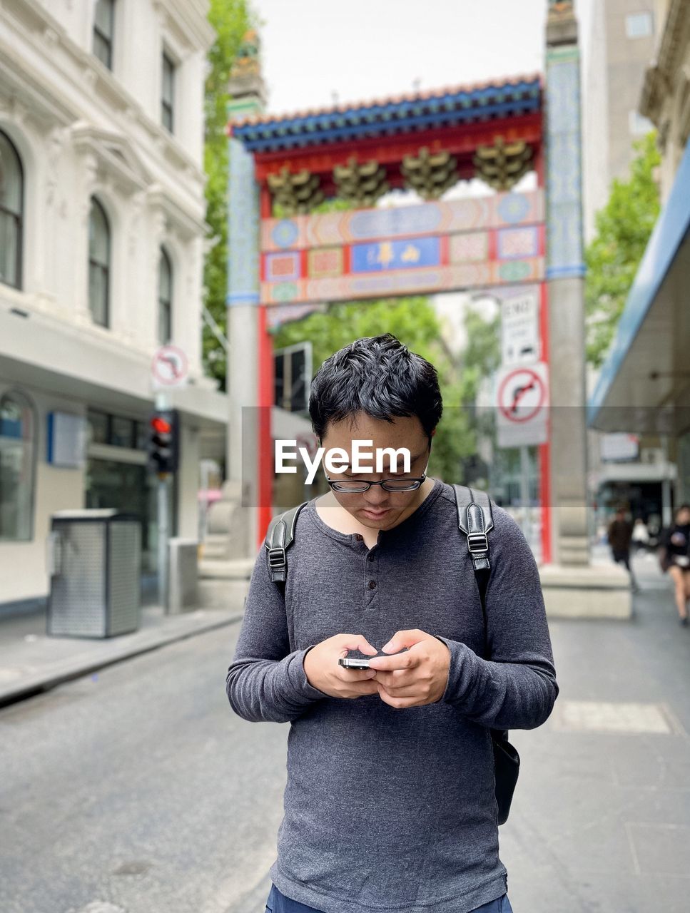 Portrait of asian man using smart phone against arch and buildings in chinatown-melbourne australia.