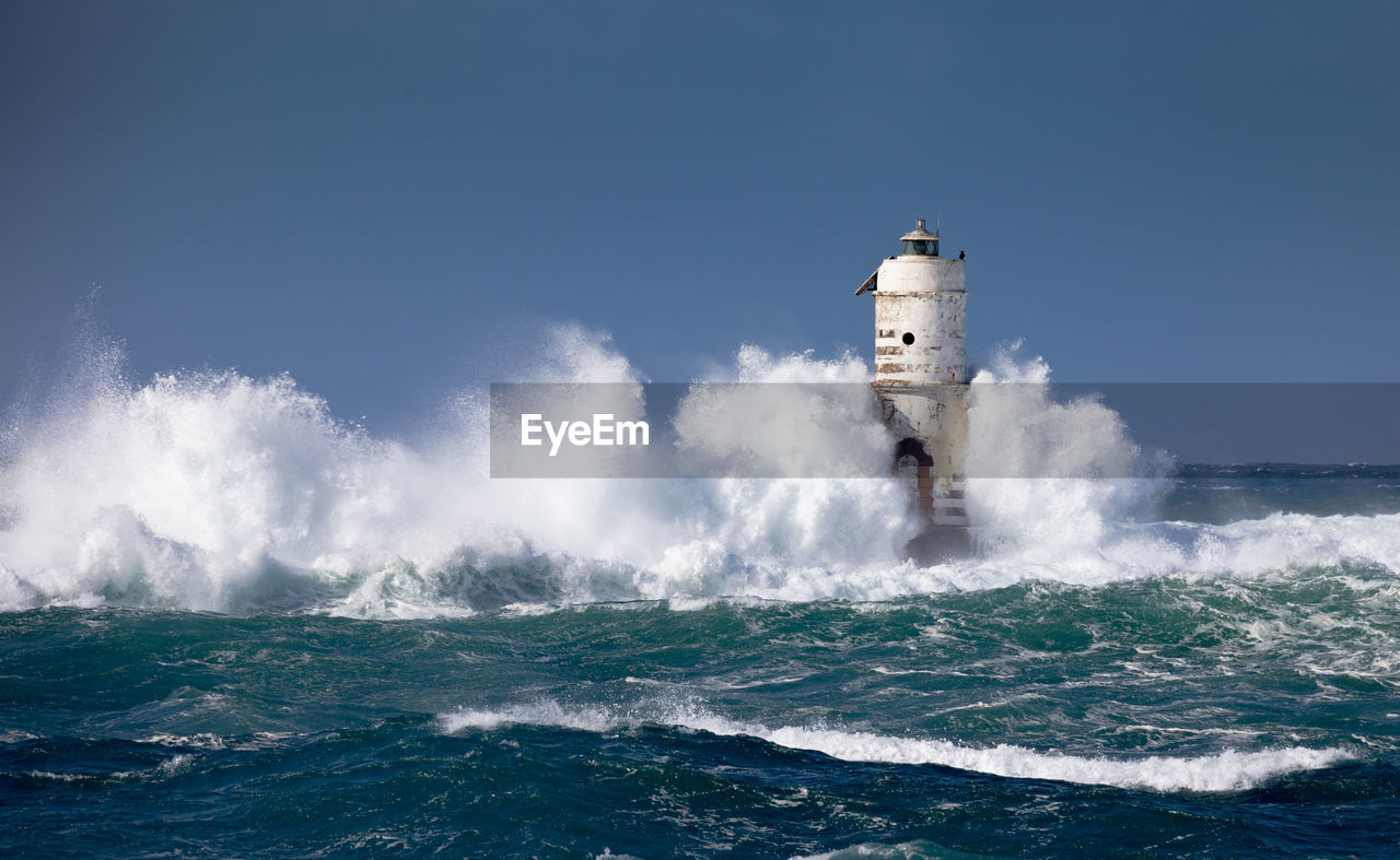 Waves splashing on lighthouse against clear sky