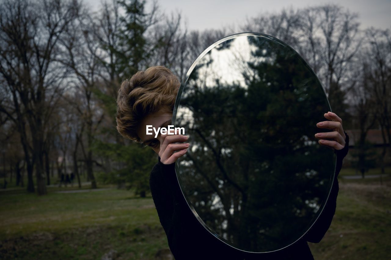 Close-up of young woman holding mirror with reflection at park