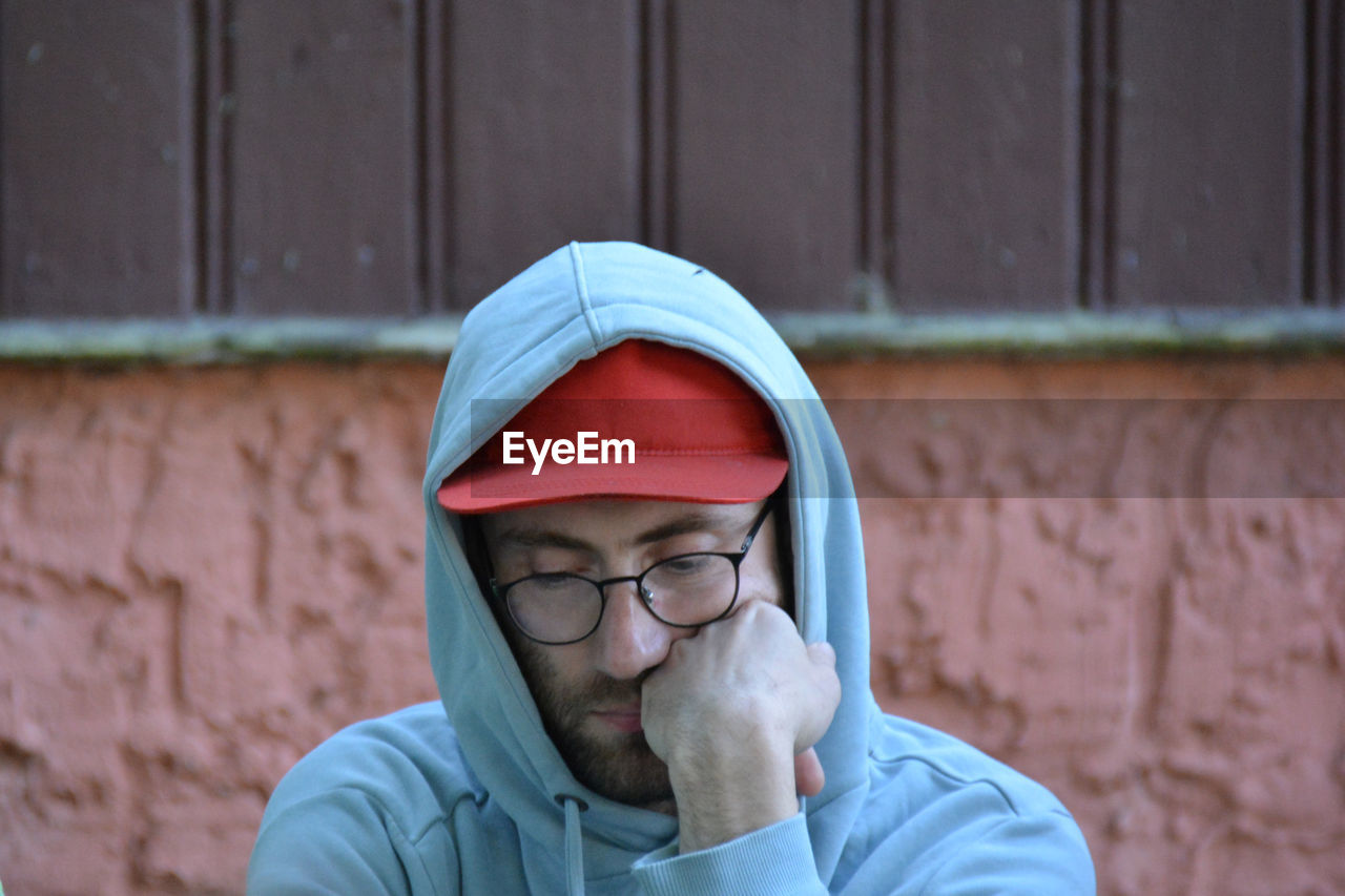 PORTRAIT OF MAN WEARING EYEGLASSES STANDING AGAINST WALL