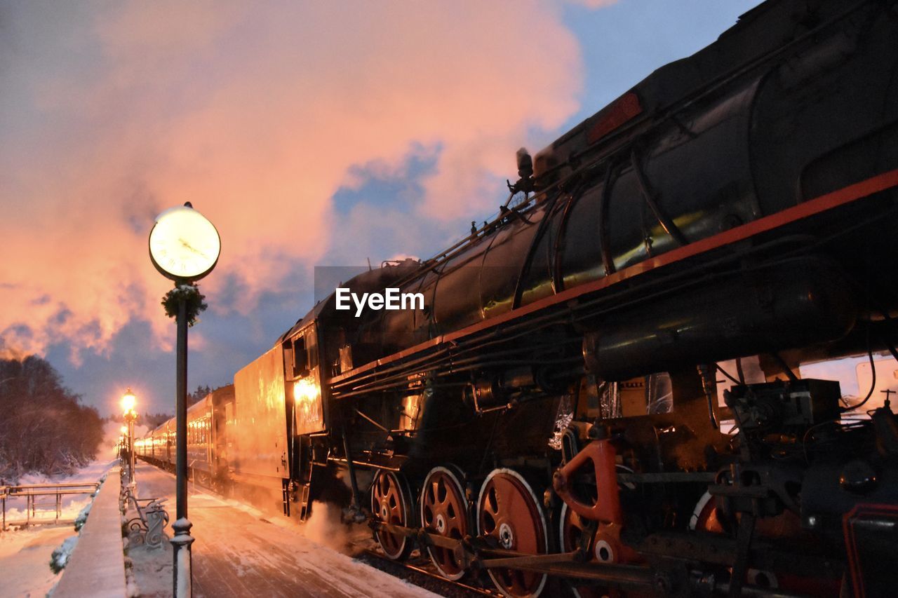 TRAIN BY ILLUMINATED RAILROAD TRACKS AGAINST SKY DURING SUNSET