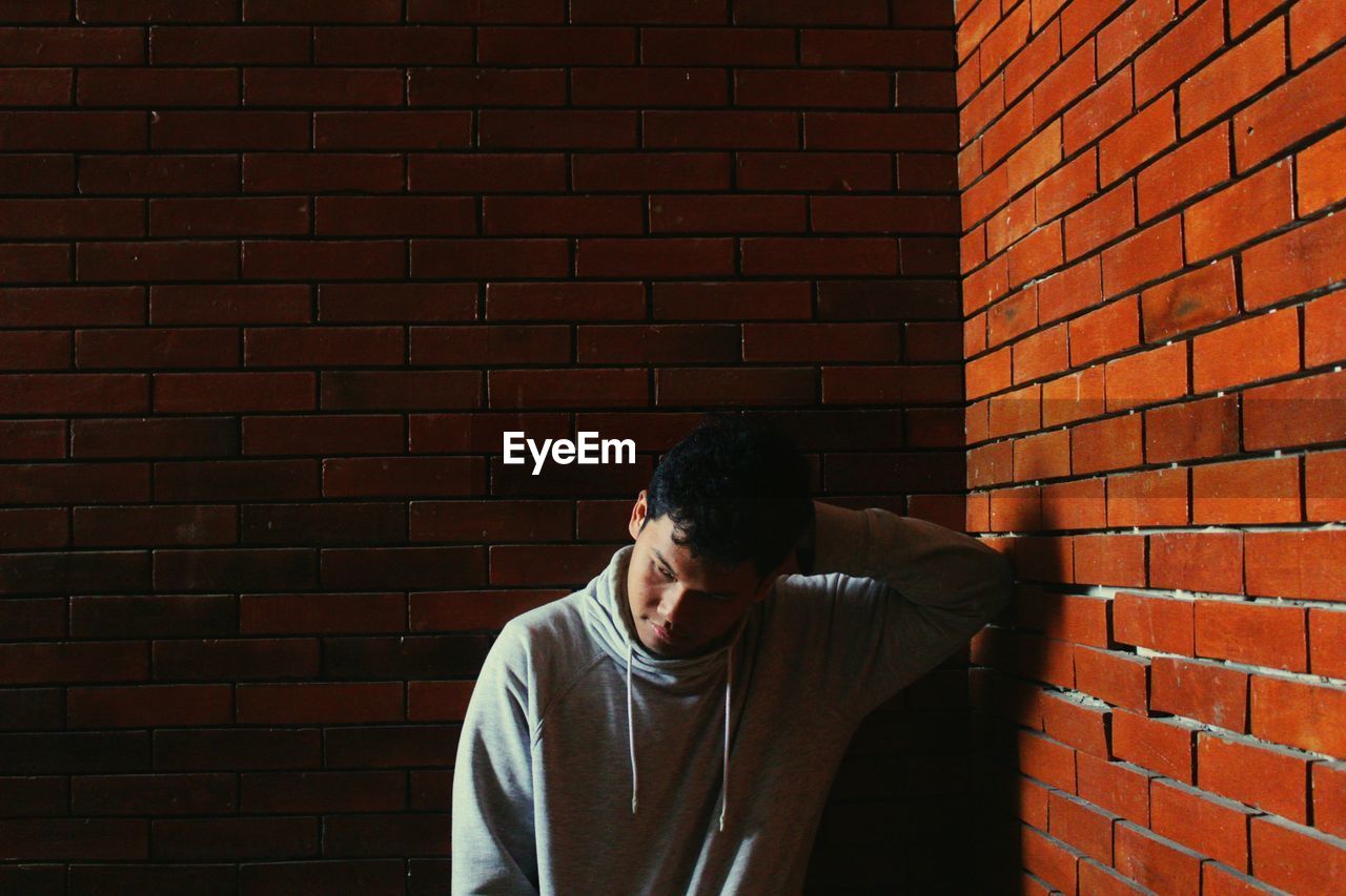 Young man standing against brick wall