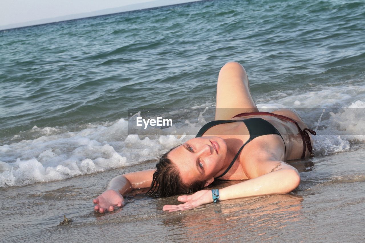 Portrait of woman lying on sand at beach
