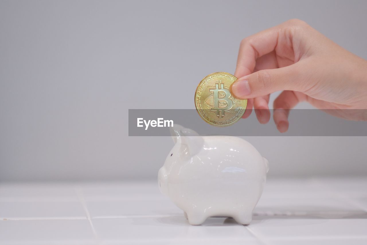 Close-up of hand putting bitcoin into piggy bank on table