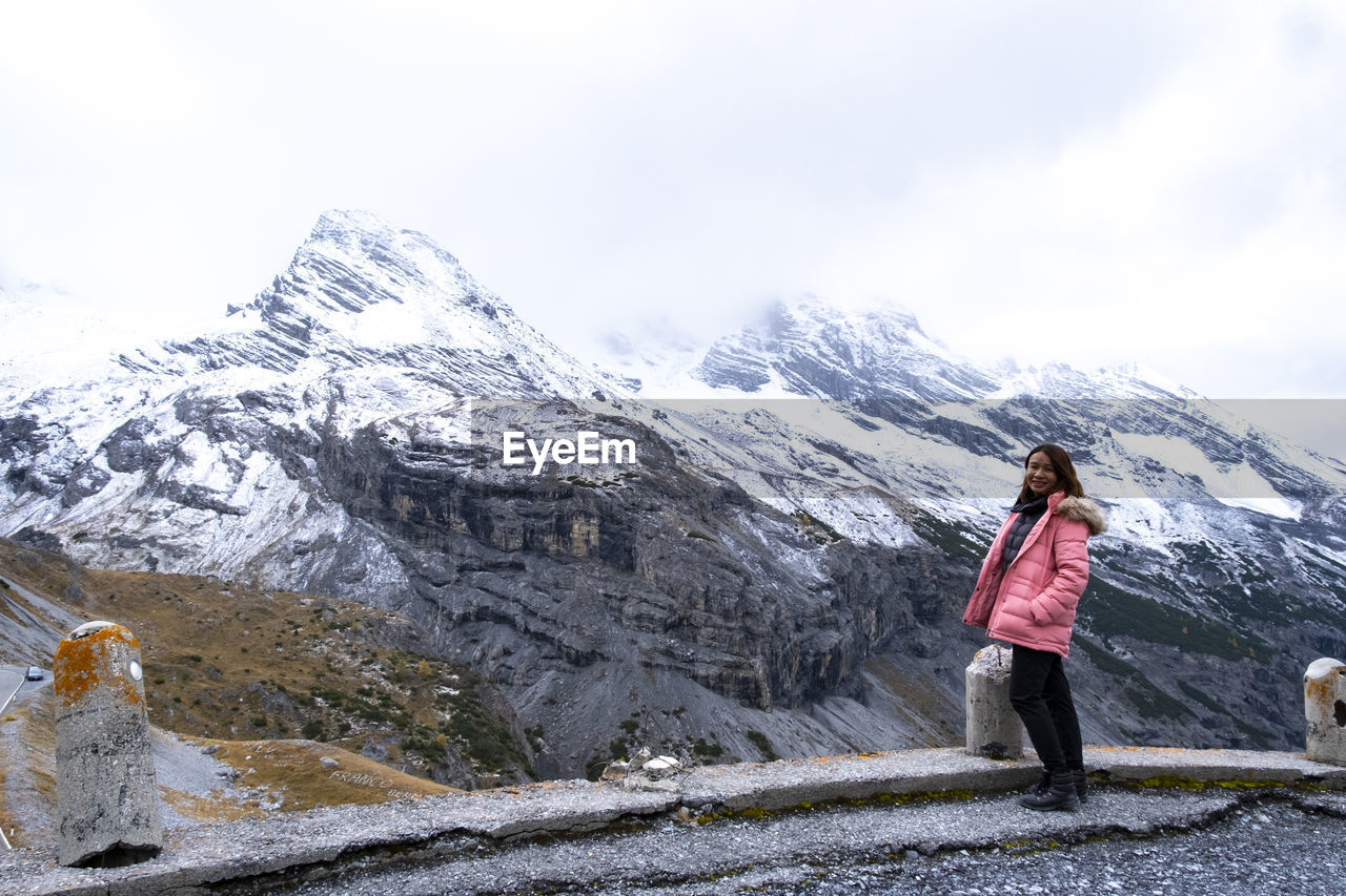 FULL LENGTH OF WOMAN STANDING ON SNOWCAPPED MOUNTAIN