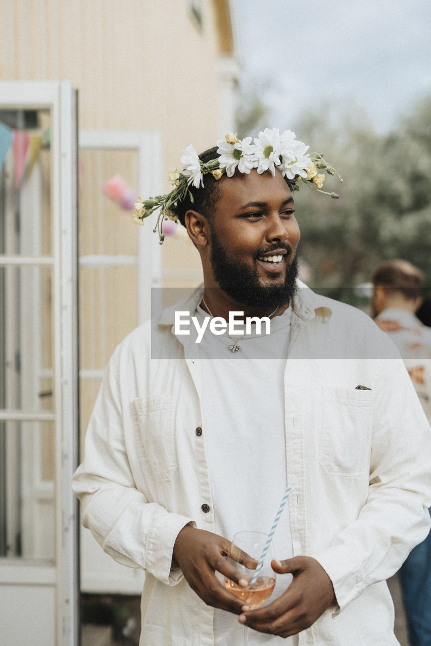 Smiling young man looking away while holding wineglass during dinner party at cafe