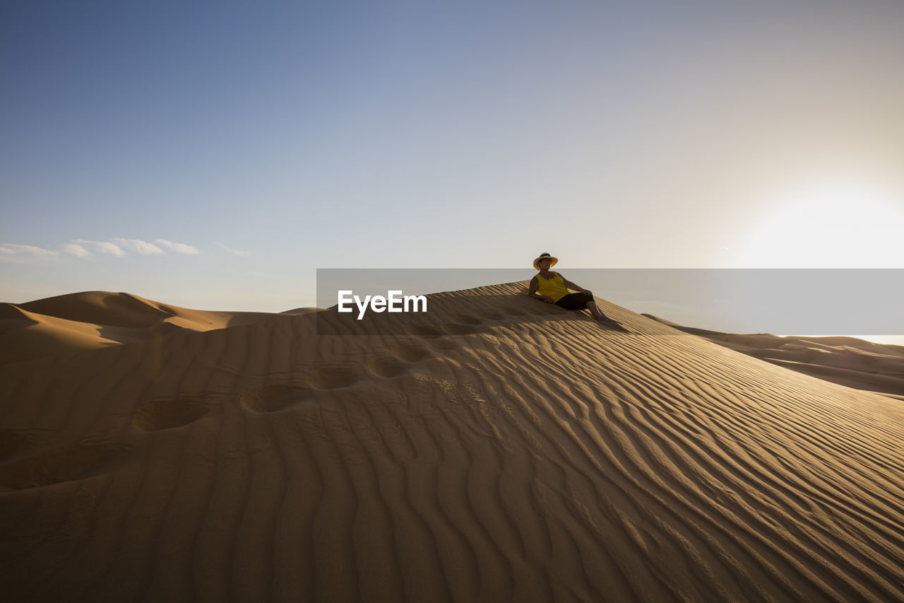 Senior woman relaxing at desert against clear sky during sunny day