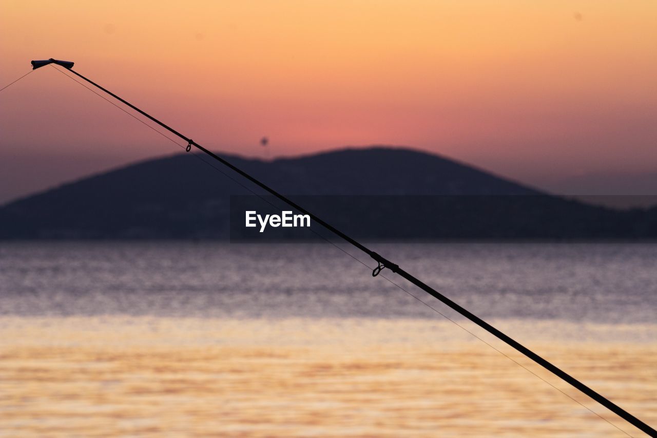 Fishing rod by sea against sky during sunset