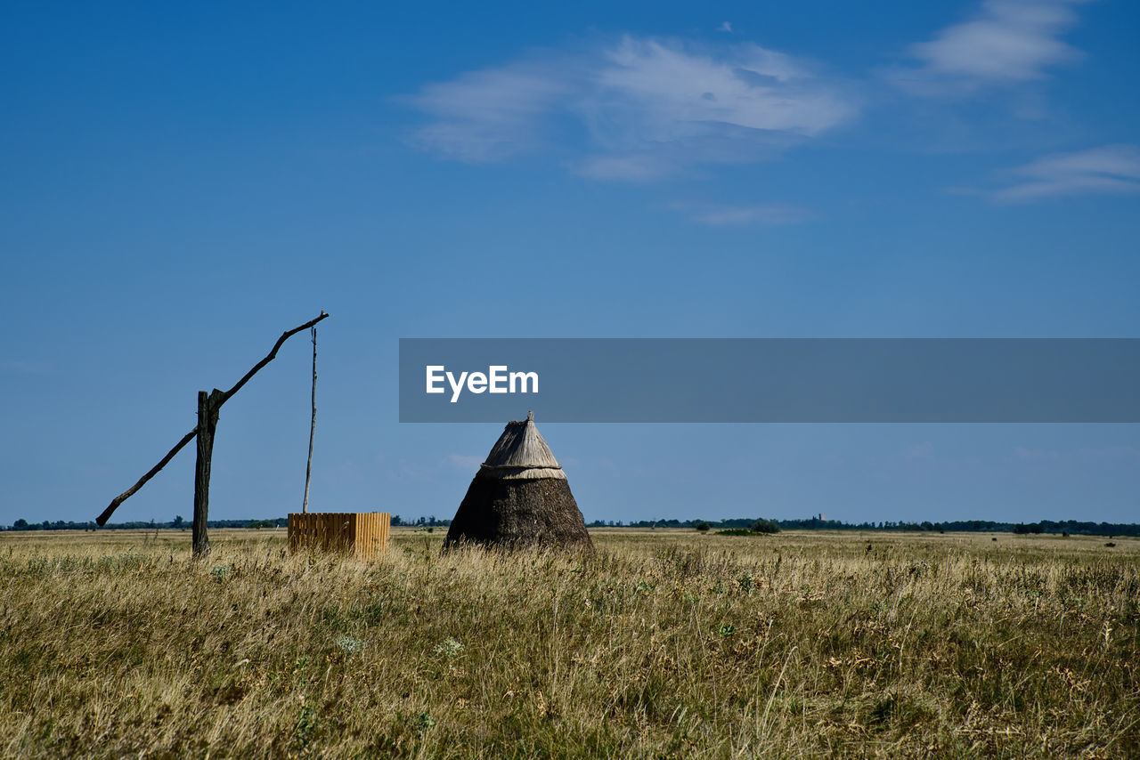 sky, landscape, field, prairie, rural area, rural scene, architecture, built structure, nature, grass, cloud, horizon, land, plant, environment, hill, wind, blue, agriculture, windmill, farm, no people, building exterior, plain, day, scenics - nature, building, abandoned, outdoors, copy space, cereal plant, tranquility, wind turbine, non-urban scene, history, agricultural building, grassland, horizon over land, wind power, beauty in nature, turbine, tranquil scene, house, renewable energy, crop, remote, the past