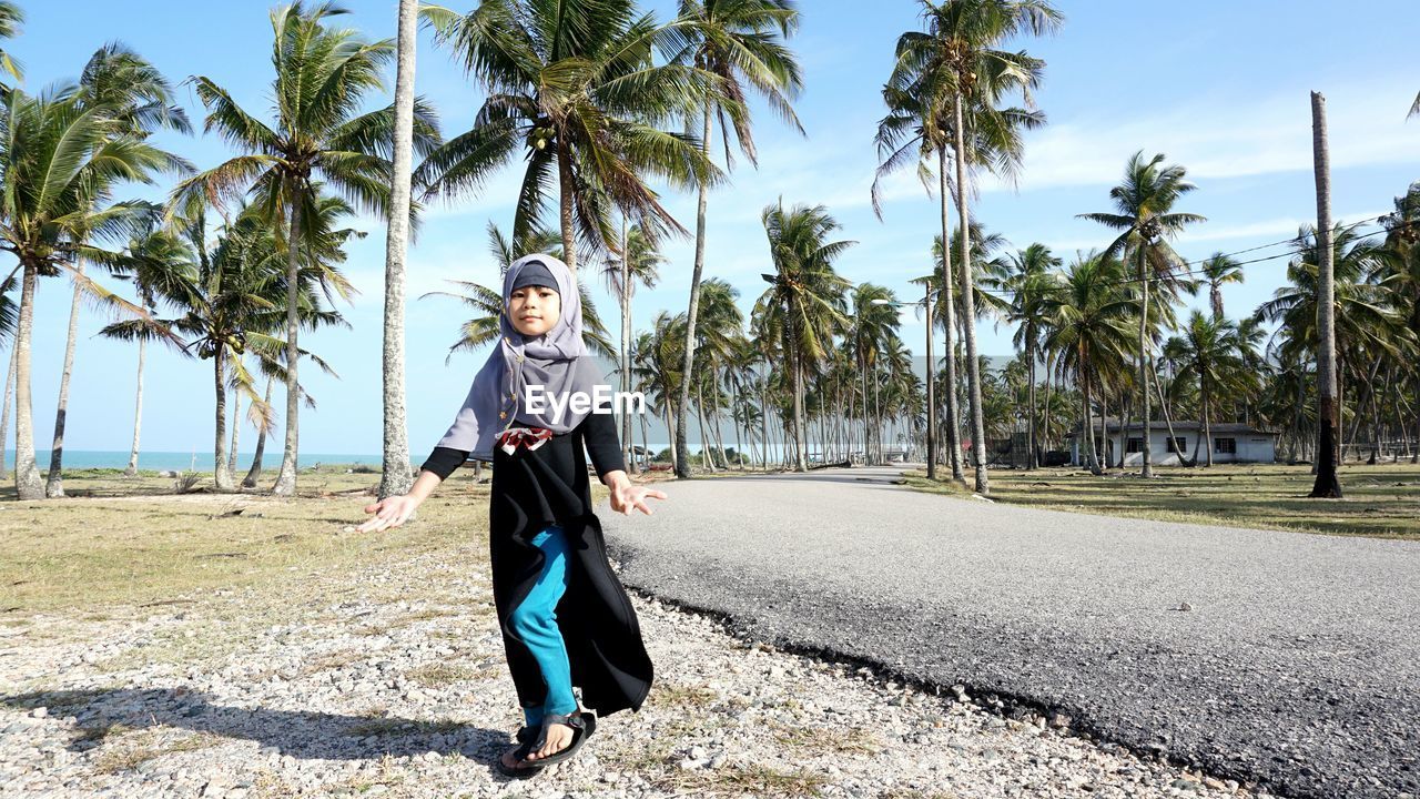 Girl walking at roadside against palm trees