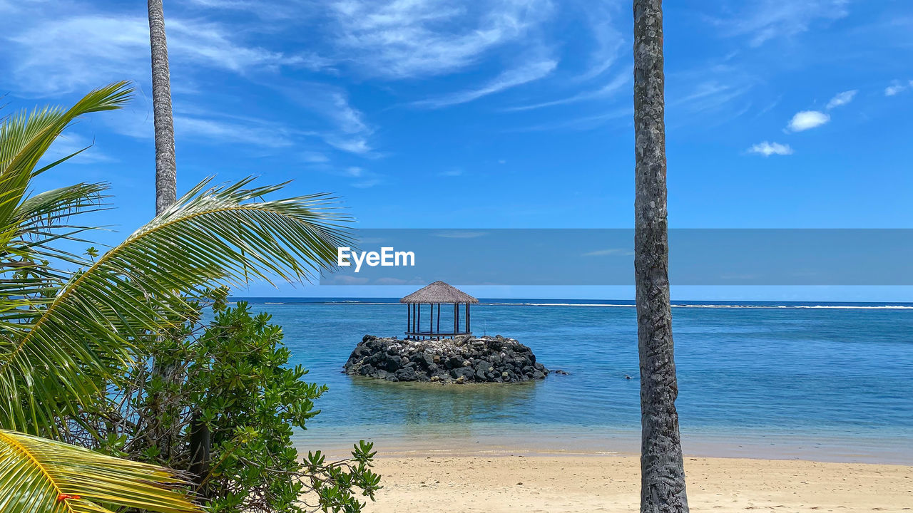 water, sea, sky, beach, land, tropical climate, palm tree, nature, tree, beauty in nature, scenics - nature, ocean, cloud, vacation, tranquility, plant, horizon over water, tranquil scene, sand, blue, horizon, travel destinations, tropics, body of water, shore, coast, architecture, holiday, no people, idyllic, day, trip, outdoors, coconut palm tree, travel, sunlight, hut, built structure, island, coastline, environment, tropical tree, tourism, bay, seascape, landscape, summer, tourist resort