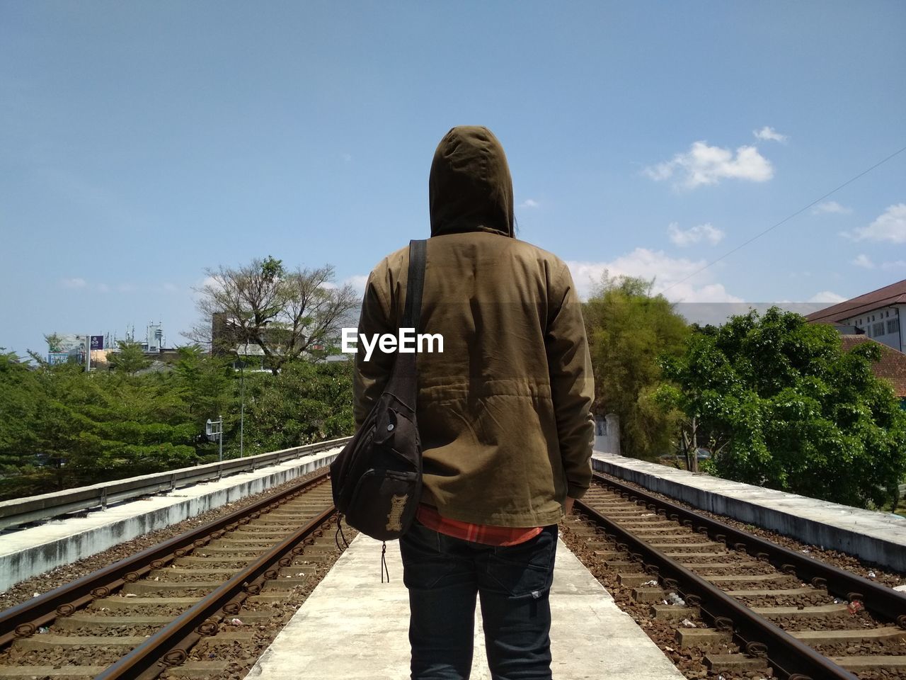 REAR VIEW OF MAN STANDING ON RAILROAD TRACKS