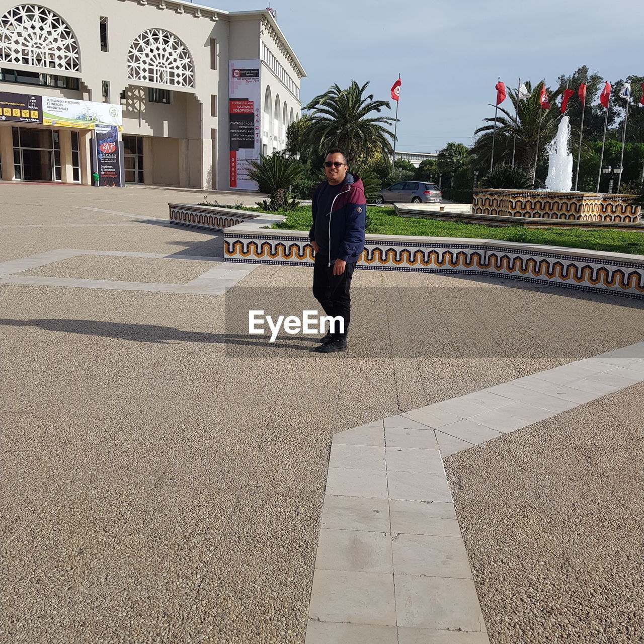 MAN STANDING ON FOOTPATH BY STREET IN CITY