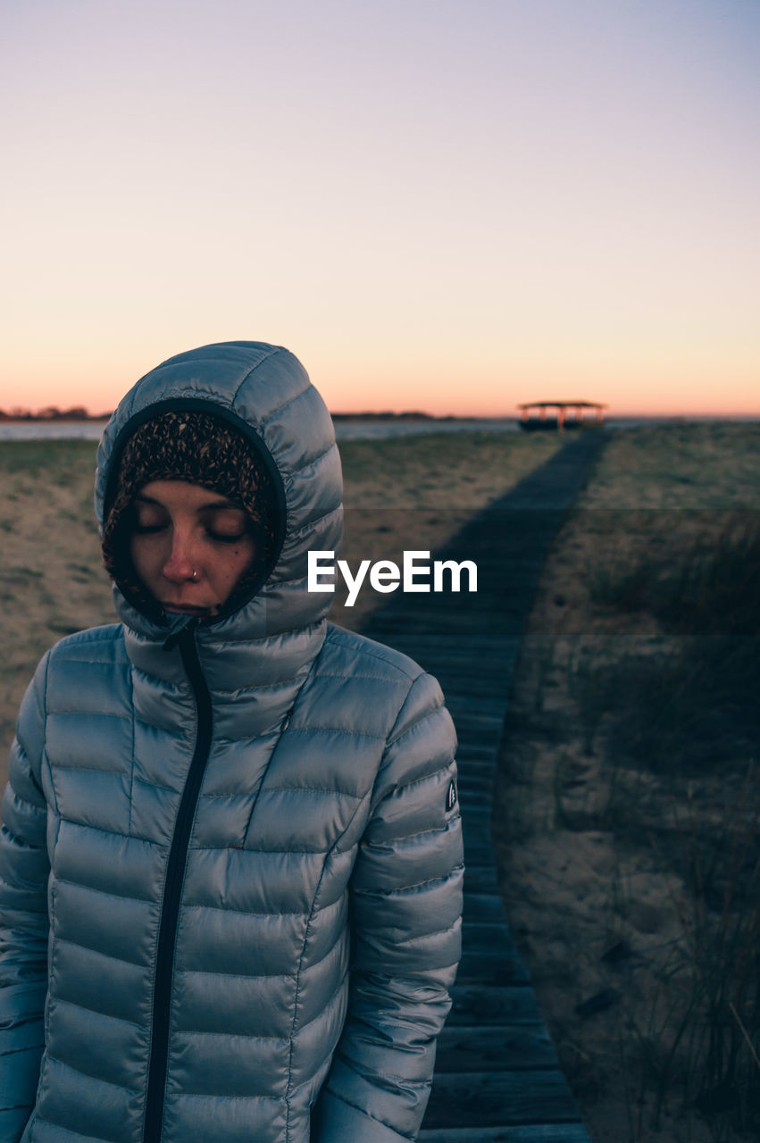 Portrait of woman standing in snow against sky during sunset