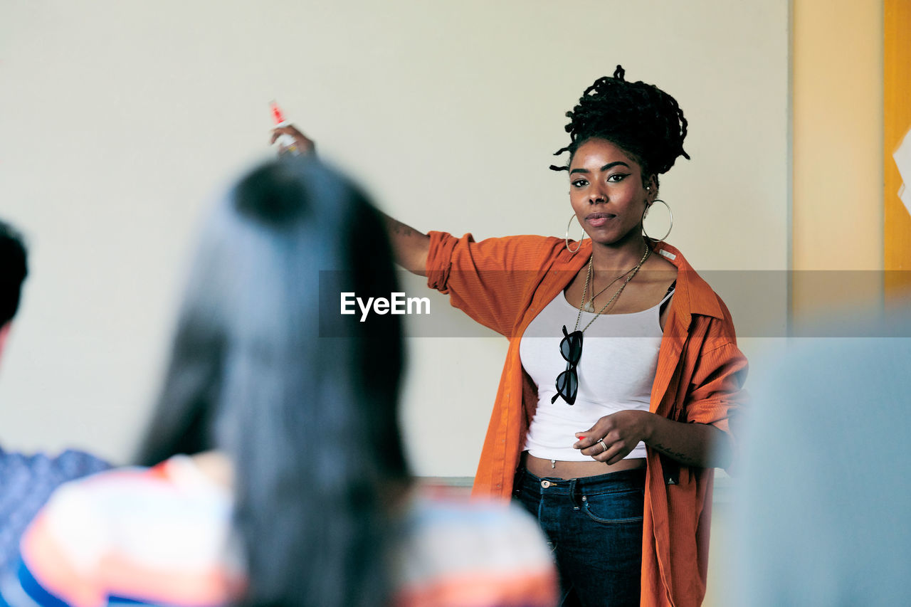 Young female teacher pointing on whiteboard while teaching students in classroom