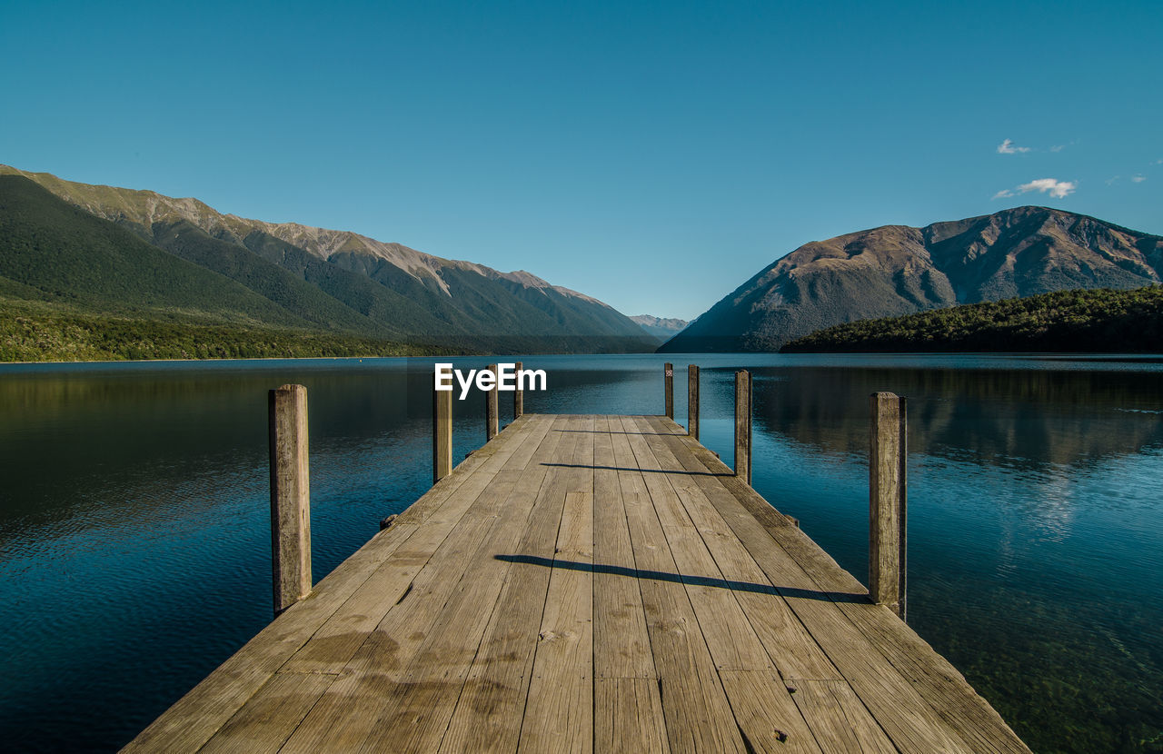 Pier over lake against clear blue sky