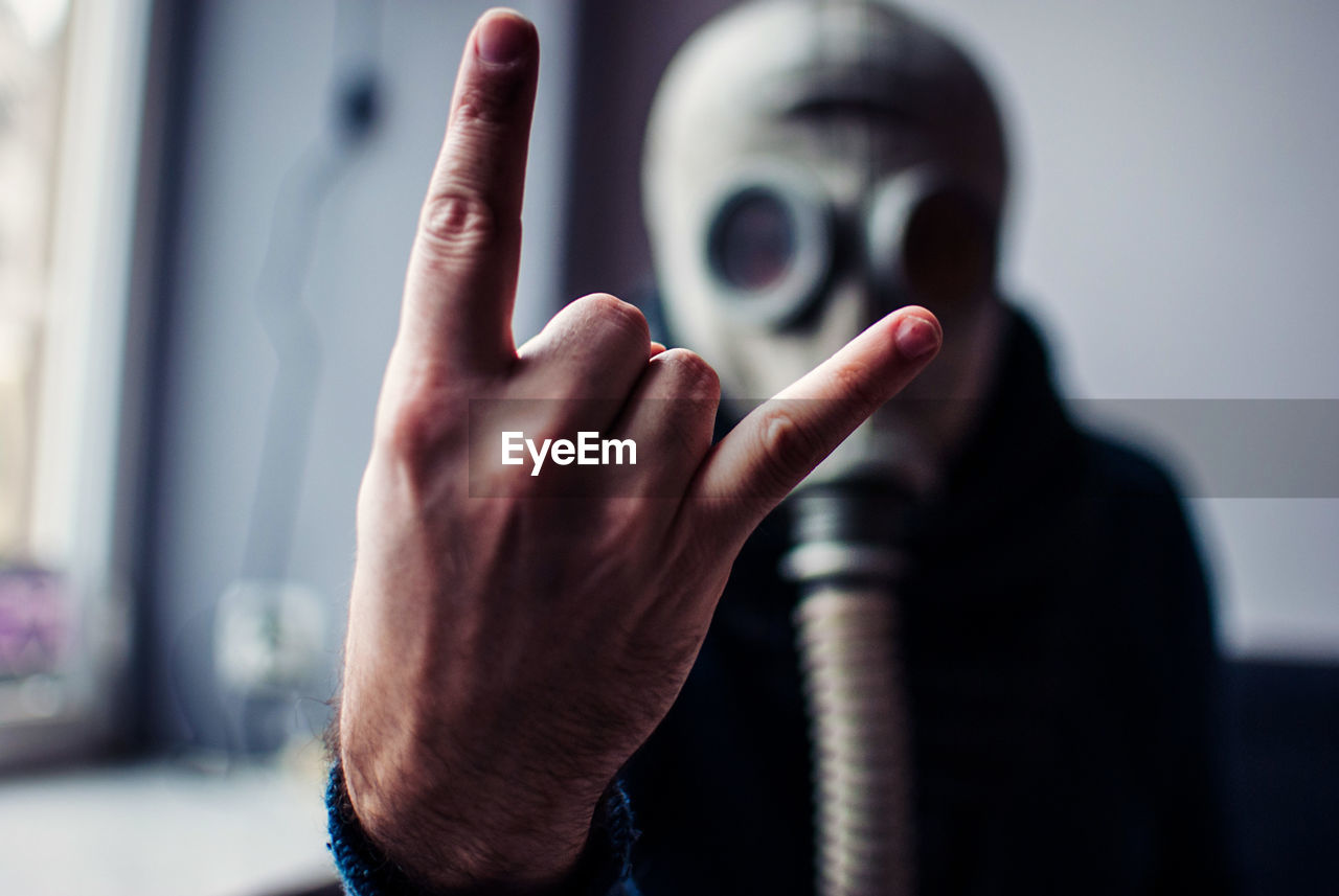 Close-up of man showing horn sign while wearing gas mask