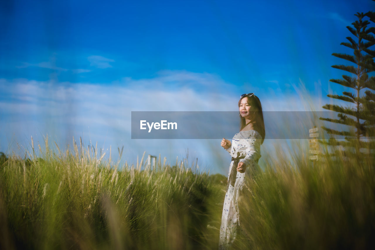 WOMAN STANDING ON FIELD AGAINST SKY