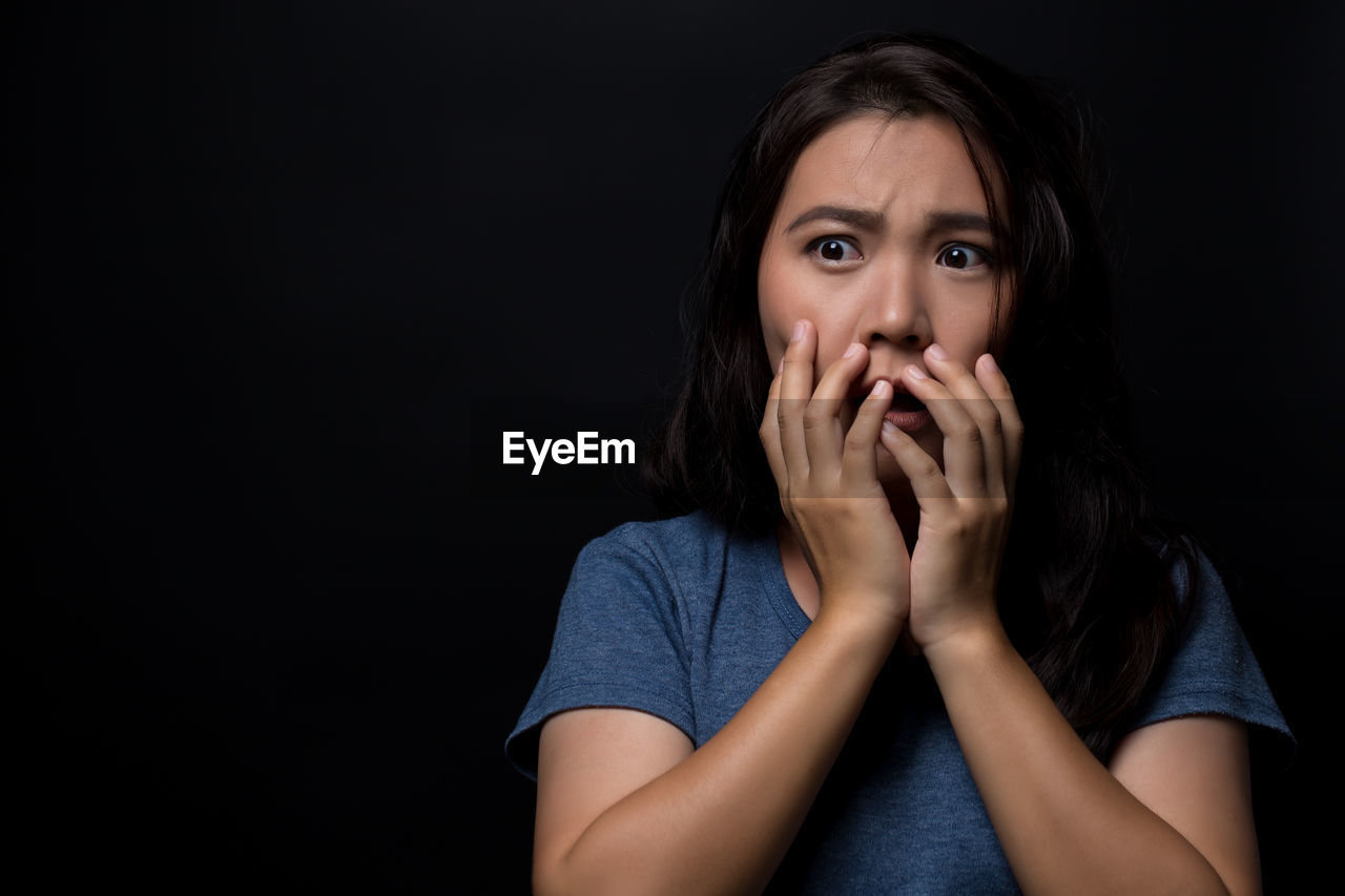 Scared young woman looking away while standing against black background