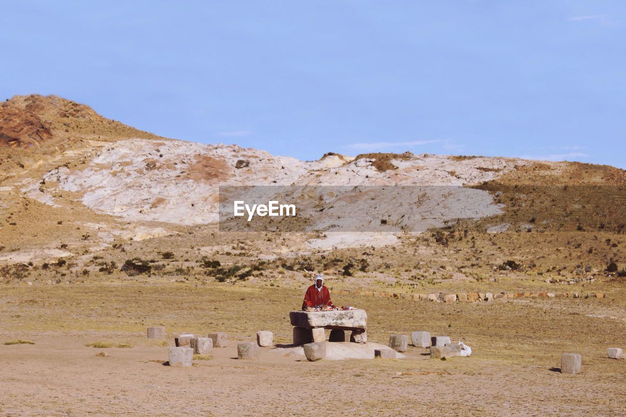 WOMAN SITTING ON LANDSCAPE AGAINST CLEAR SKY