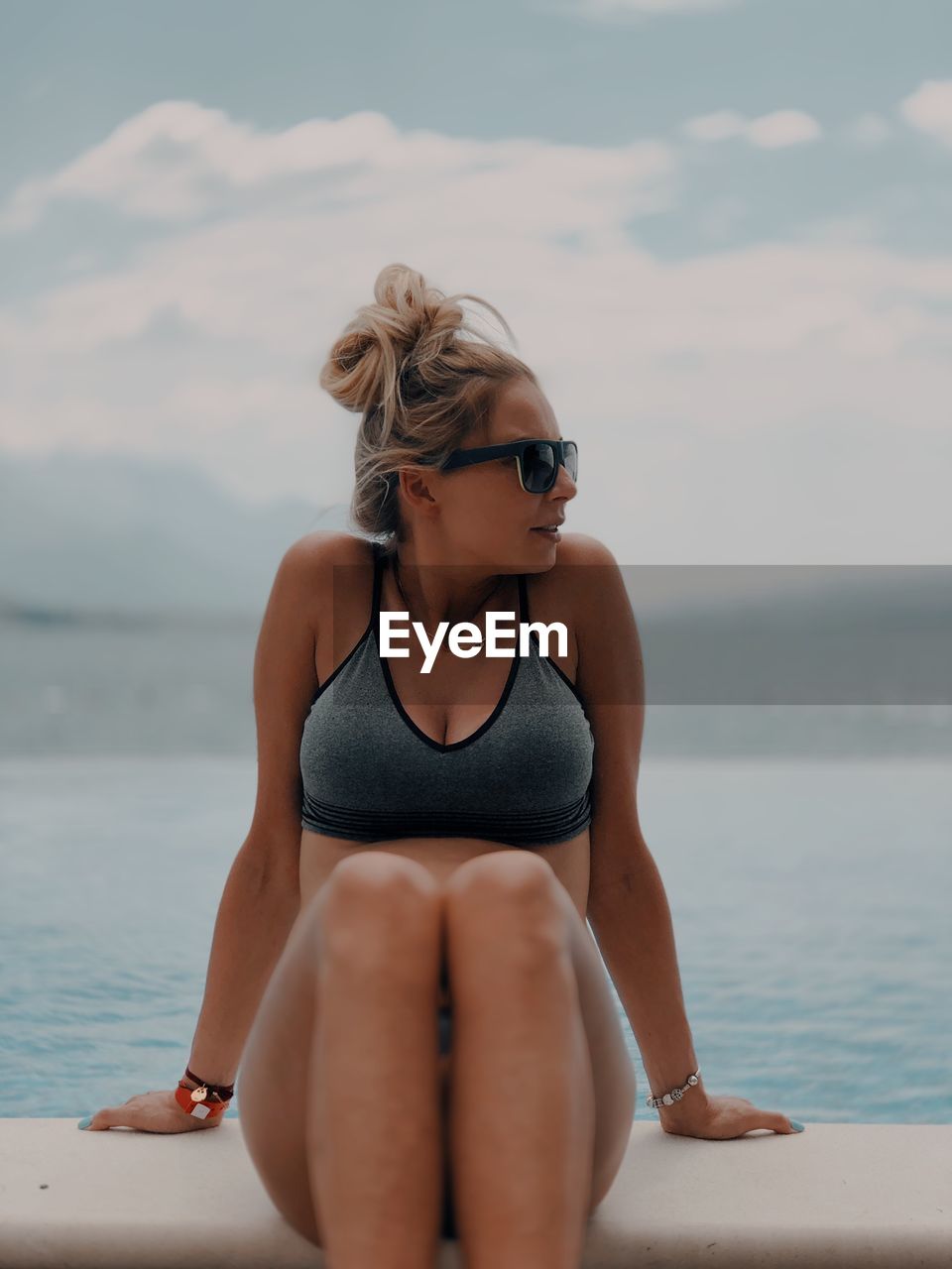 Woman looking away while sitting against sea