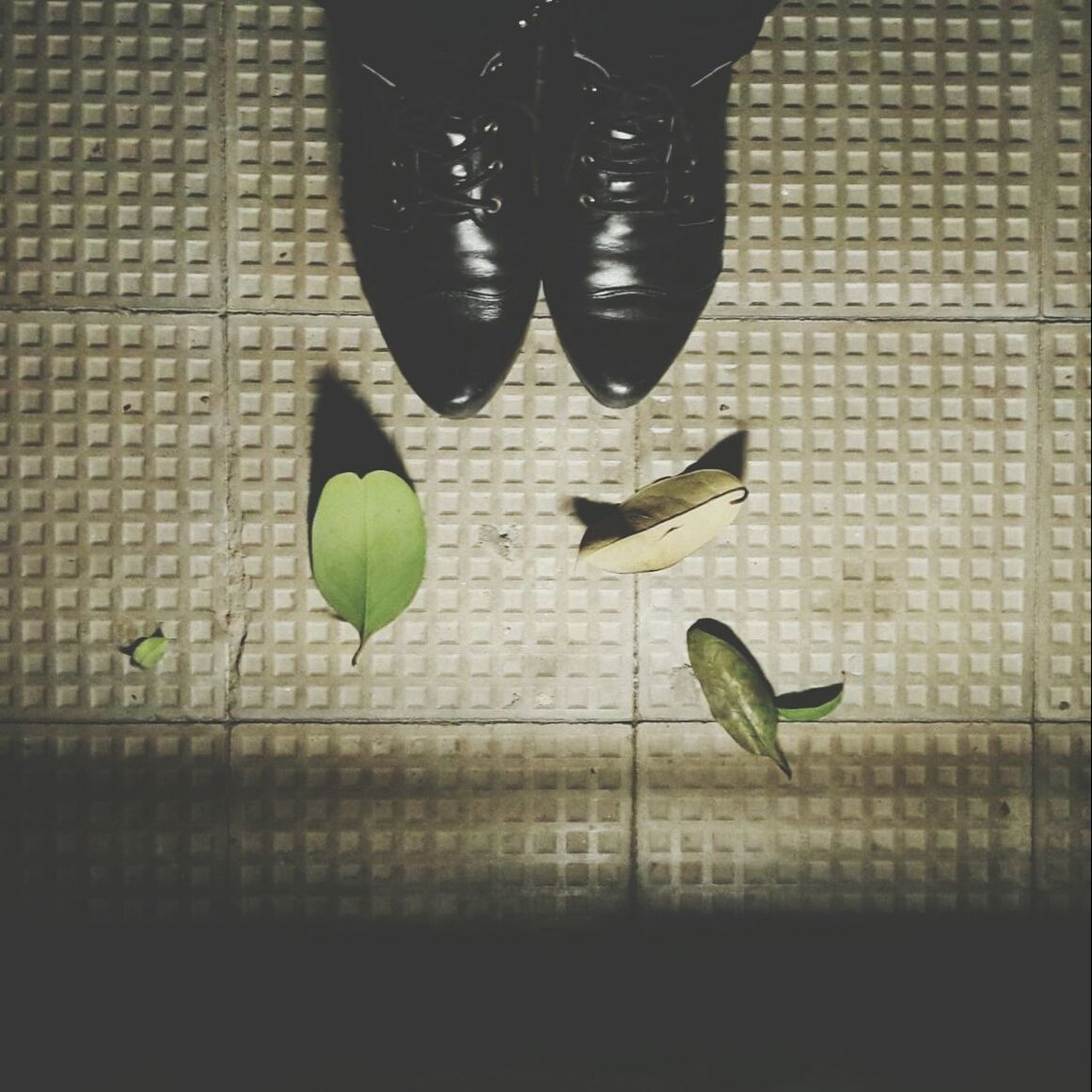 Cropped shoes and leaves on tiled floor