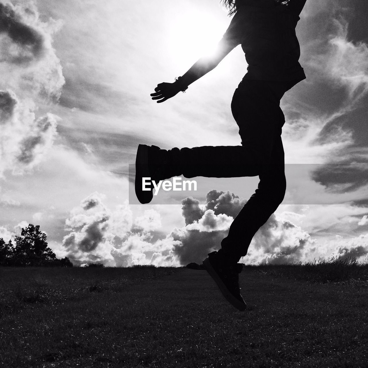 Silhouette low section of girl jumping on landscape against sky