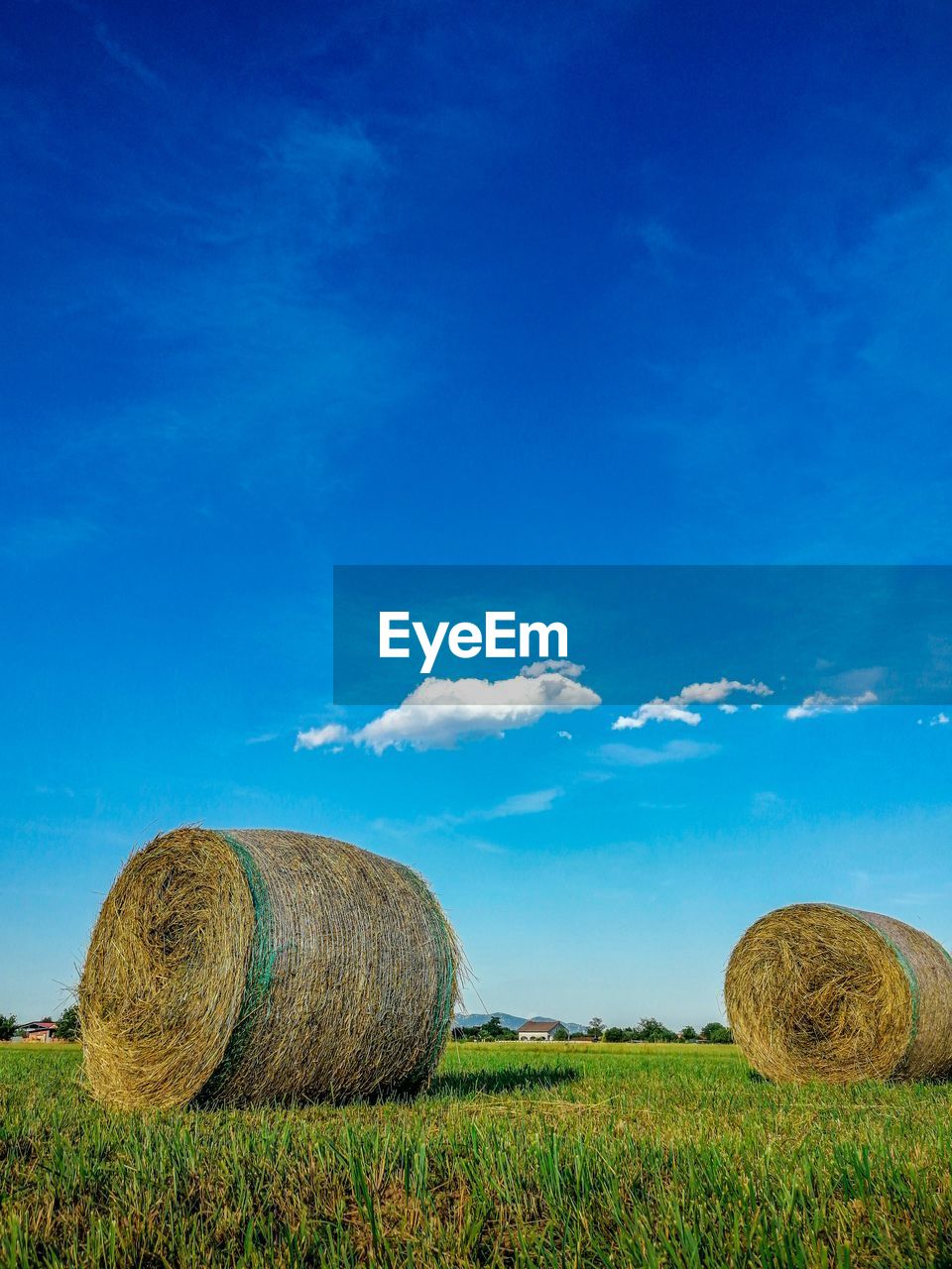 Hay bales on field against blue sky