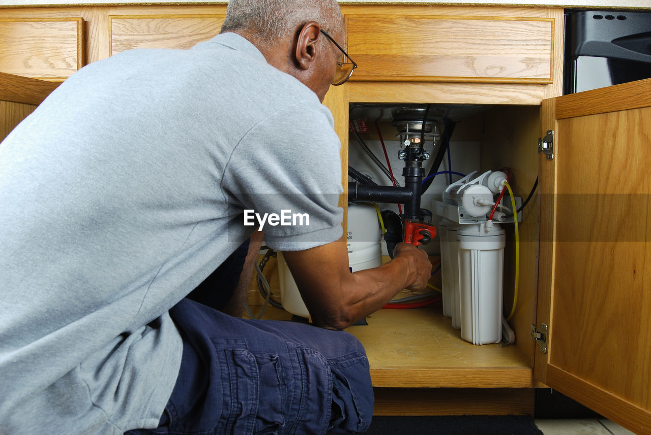 Mature man with wrench tighten pipes under sink at home